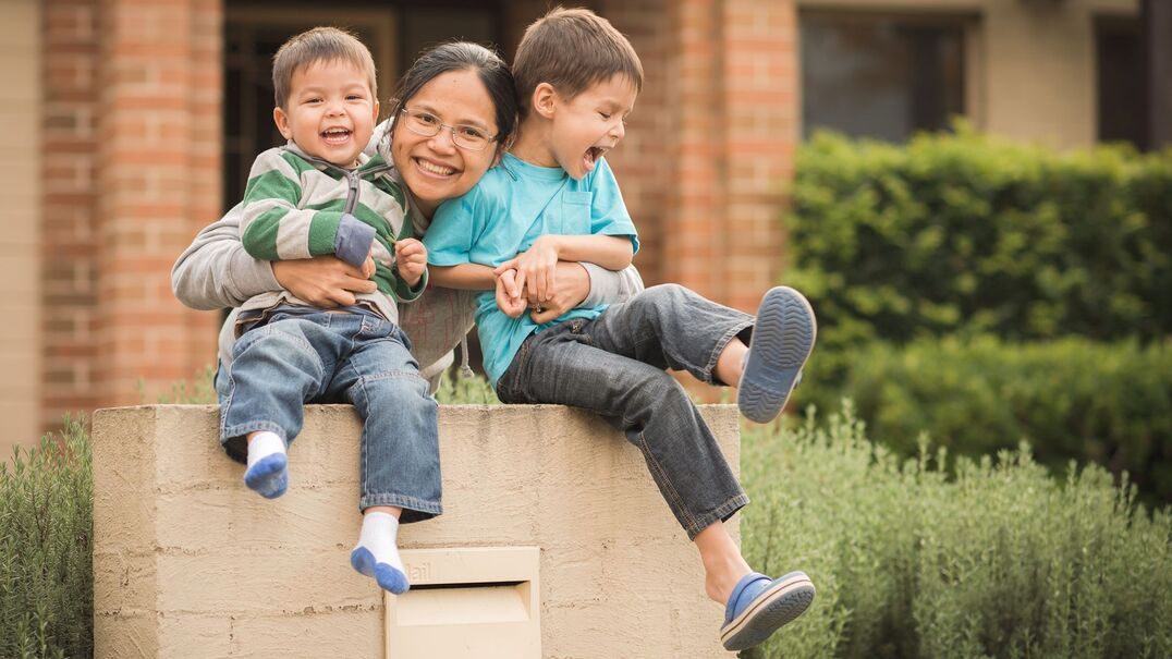 Mum and two kids sitting on a brick letterbox smiling