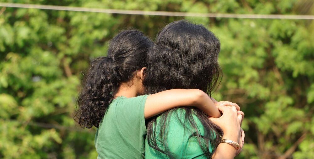 The back of two girls in green tops embracing each other
