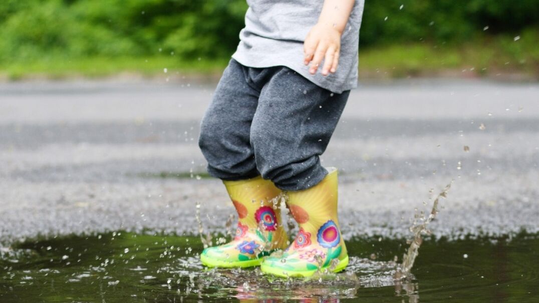 Child wearing gumboots splashing in puddle
