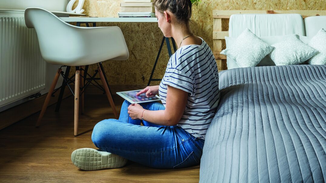 Teenage girl sitting on bedroom floor using an iPad