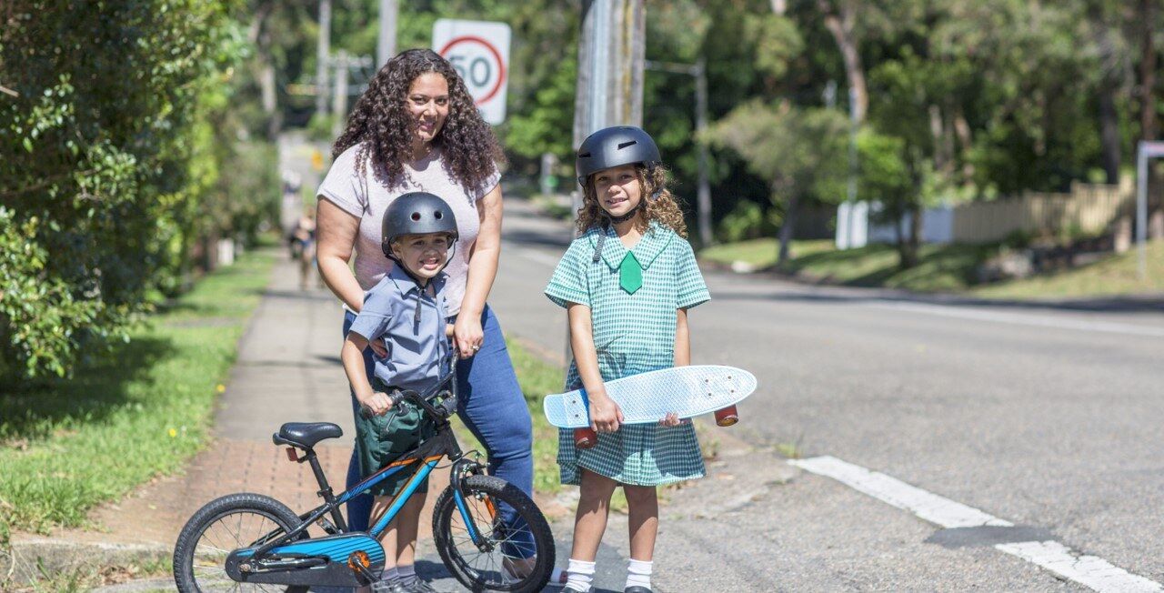 Mum and two children outside holding a bike and skateboard