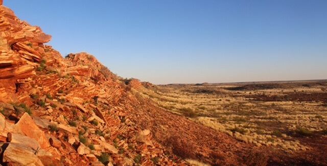 red rocky ridgeline opening into dry srubby country under a blue sky