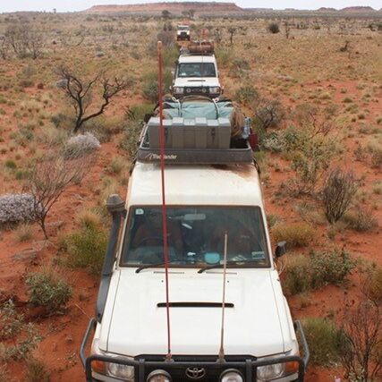 Four wheel drives loaded up and driving through the red dirt desert in convoy to take community members out on country.