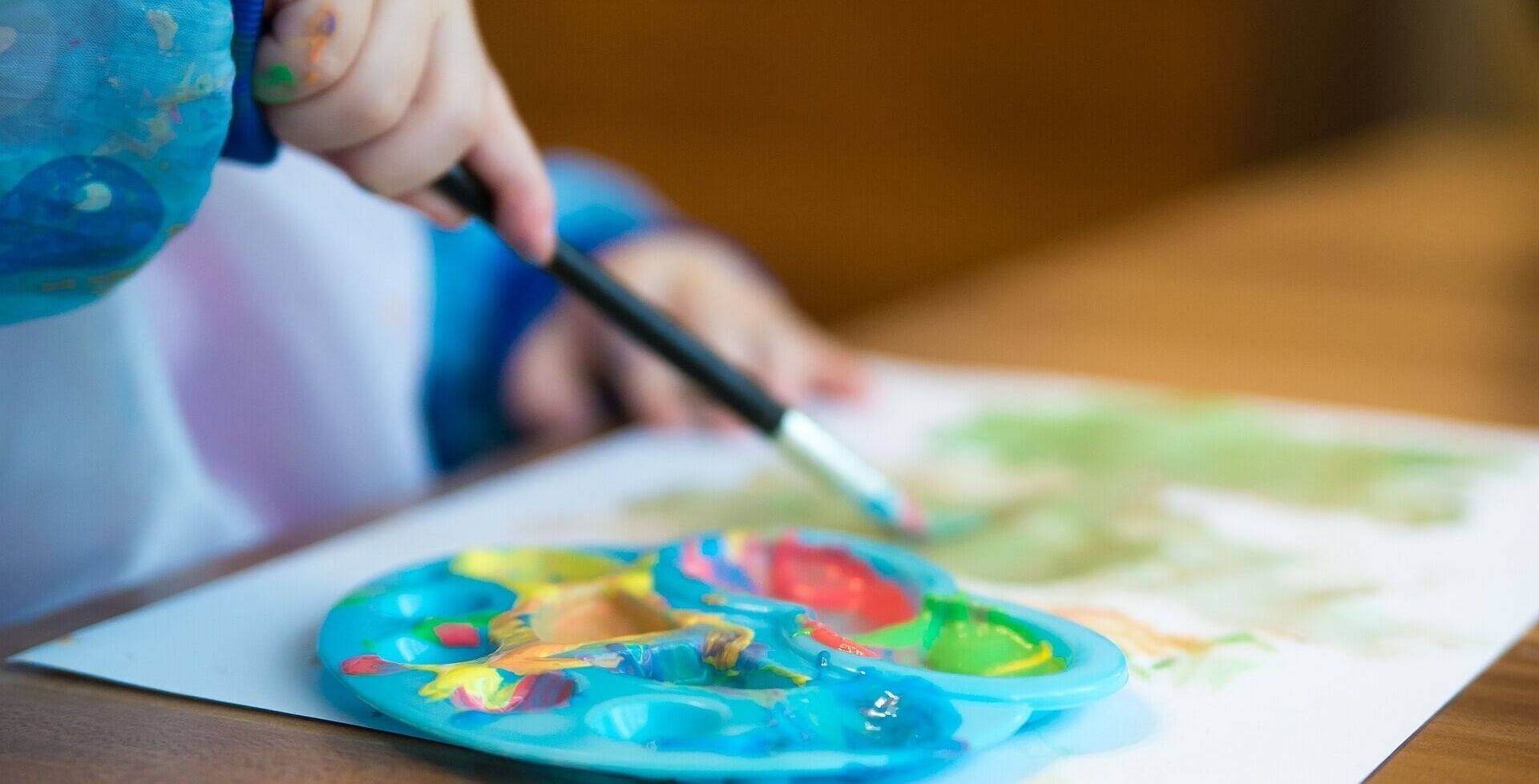 toddlers hands painting a piece of paper with a paintbrush