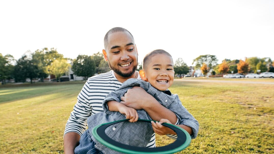 Father holding child having fun in the park with a frisbee