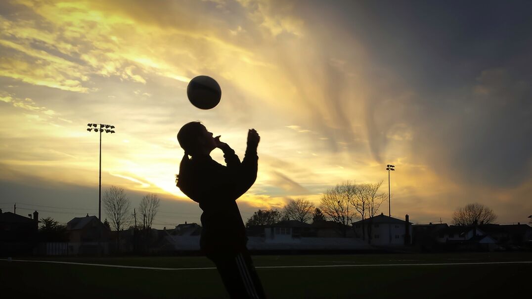 Sienna silhouetted in dusk light playing with her soccer ball at the oval.