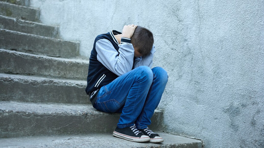 12 year old boy sitting on concrete stairs head in his hands.