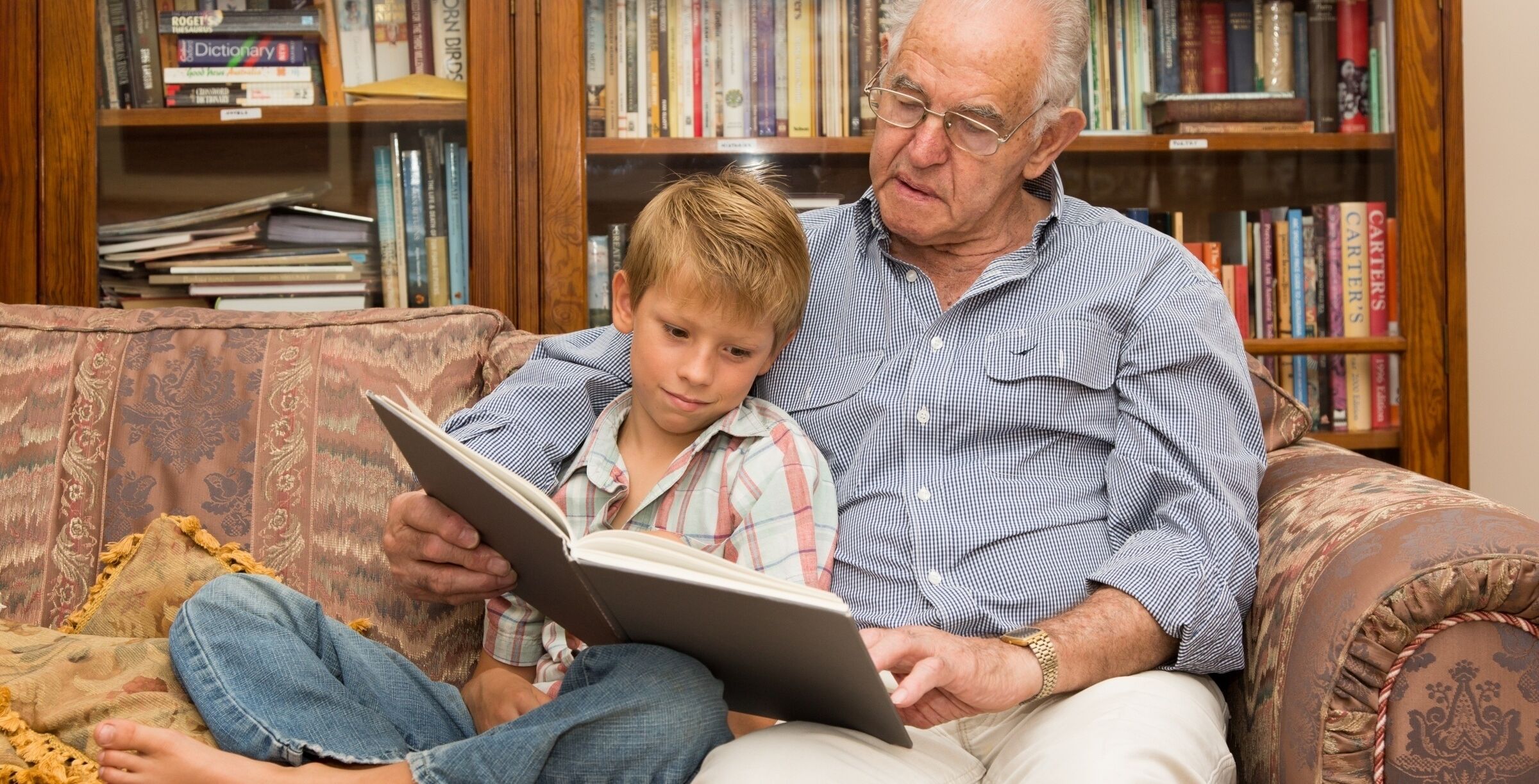 Male grandparent sitting reading to boy grandchild