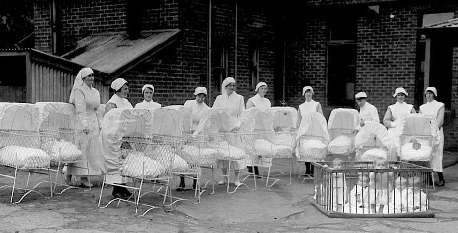 Historical picture of nurses standing outside with babies in cots