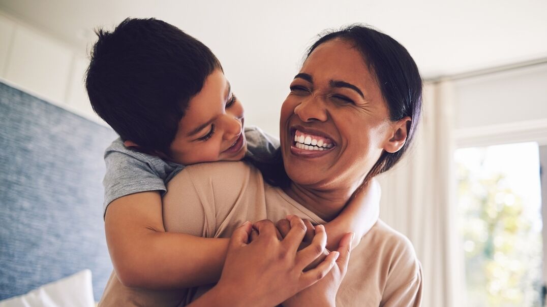 Mother and son embrace and laugh at home
