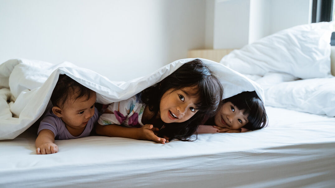 Three siblings hiding under bed covers