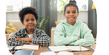 Two yoiung siblings sit at a desk and work on the homework arrayed in front of them.