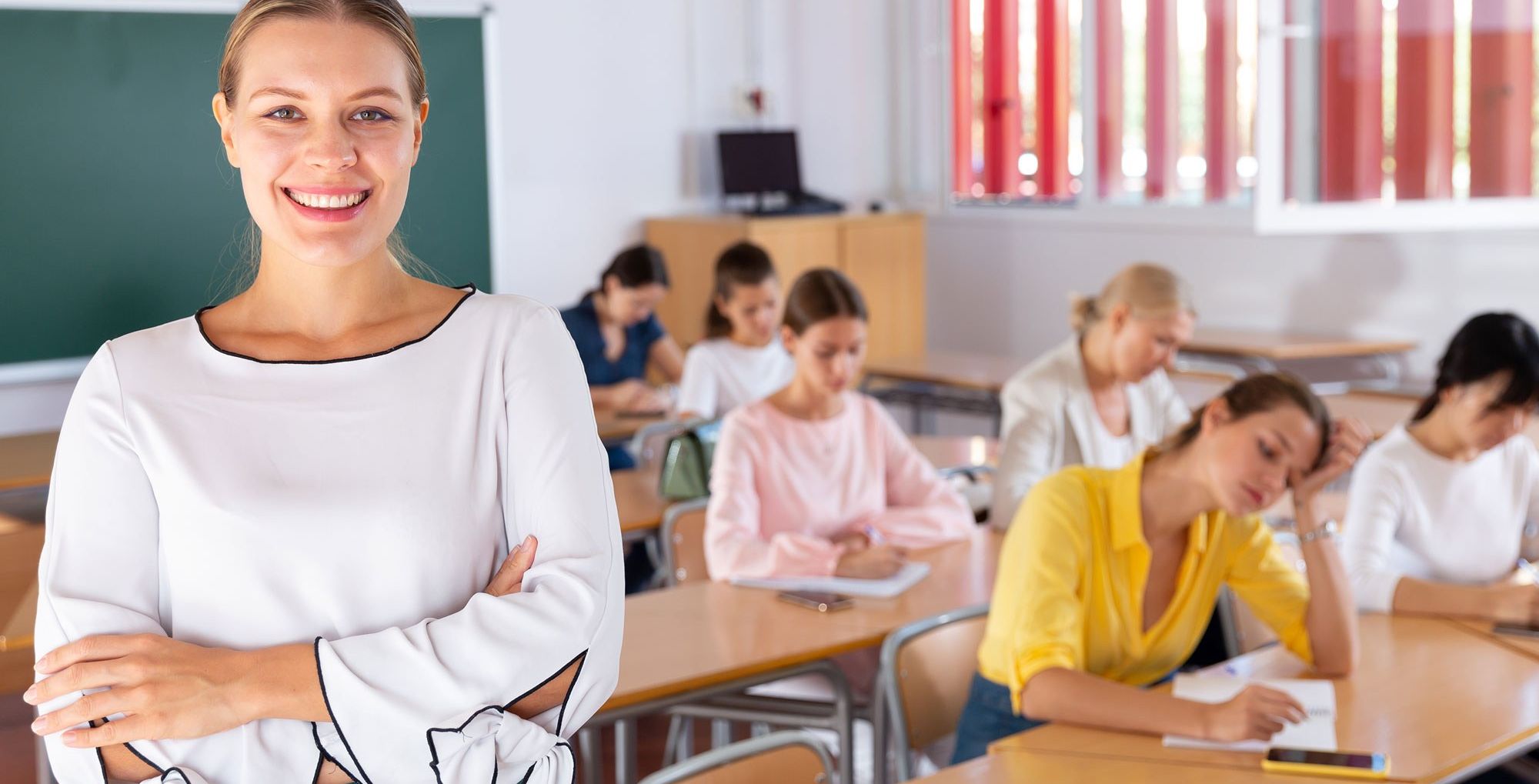 Female teacher smiling with students working at tables in background