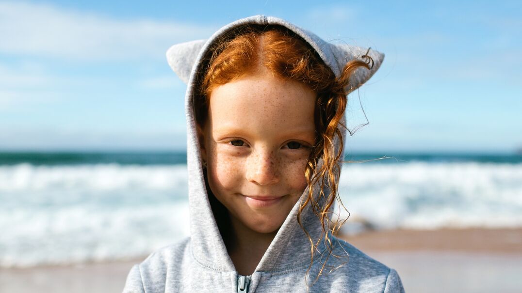Young girl with red hair on the beach smiling at the camera