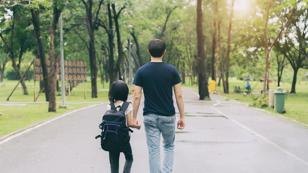 An adult and child walking side by side in a park
