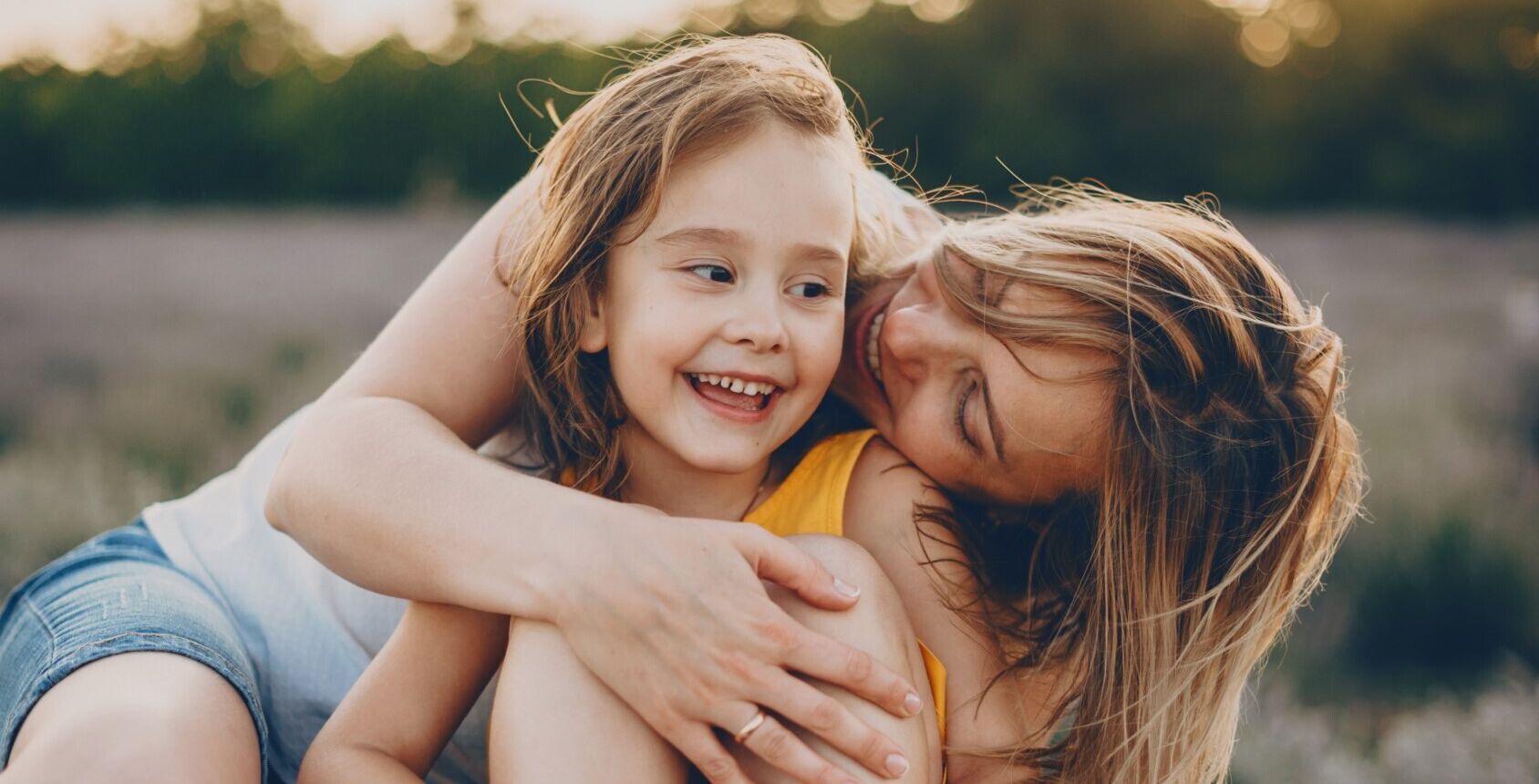 Lady hugging a smiling child in a field