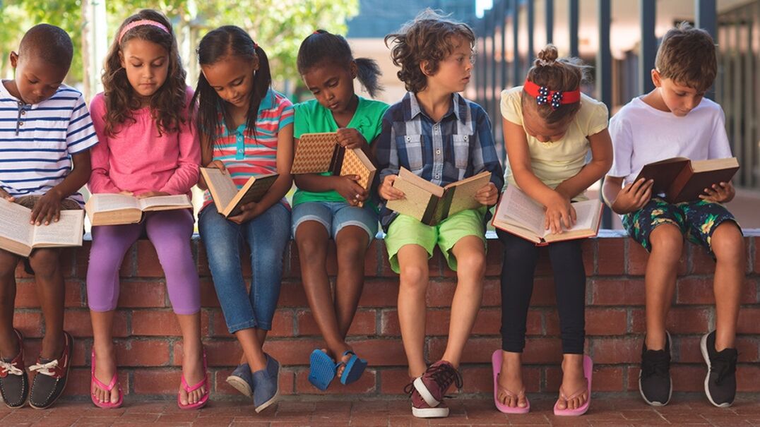 Seven children sitting on brick ledge reading books