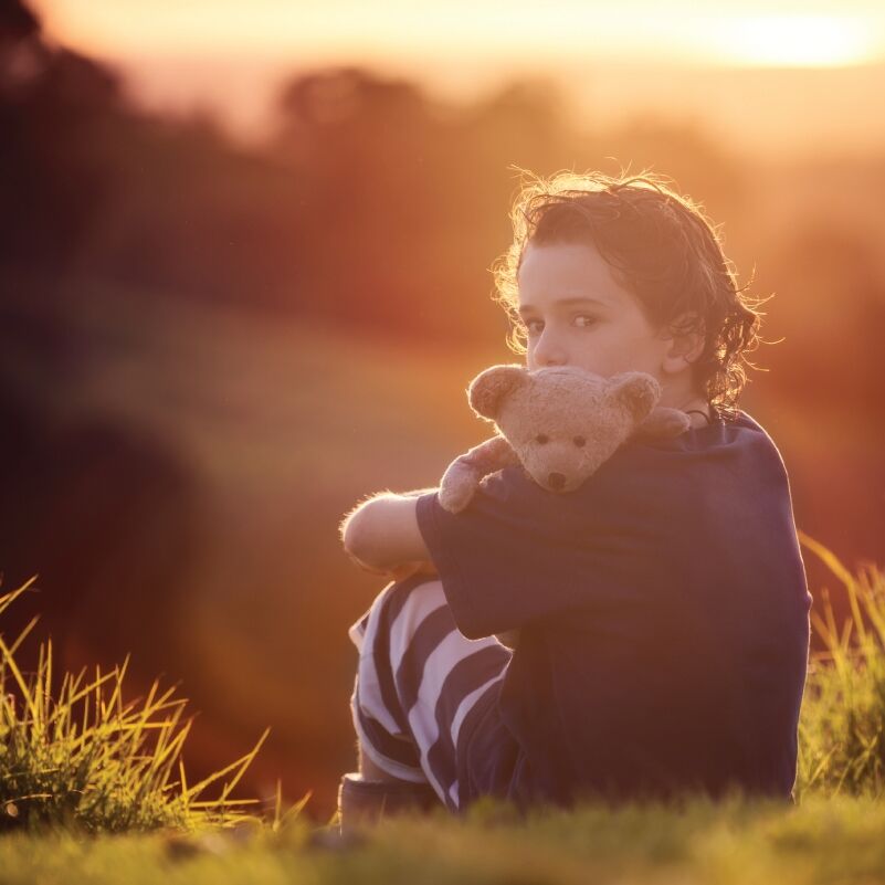 boy sitting outside holding a teddy bear