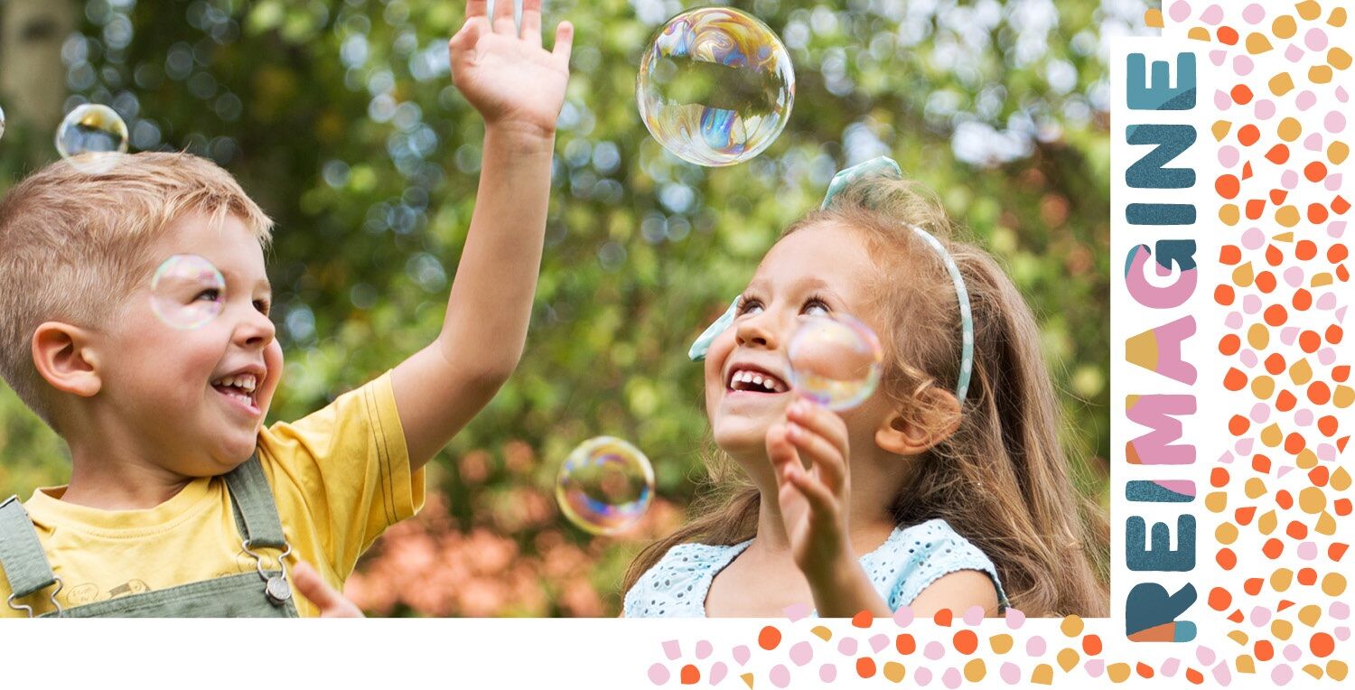 Children playing with bubbles with the word reimagine