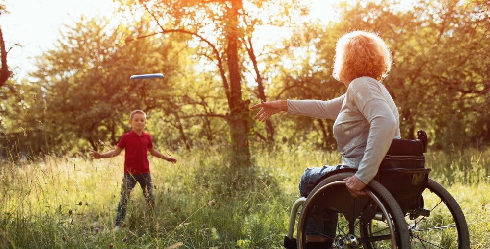 Woman in wheelchair throwing frisbee to young boy