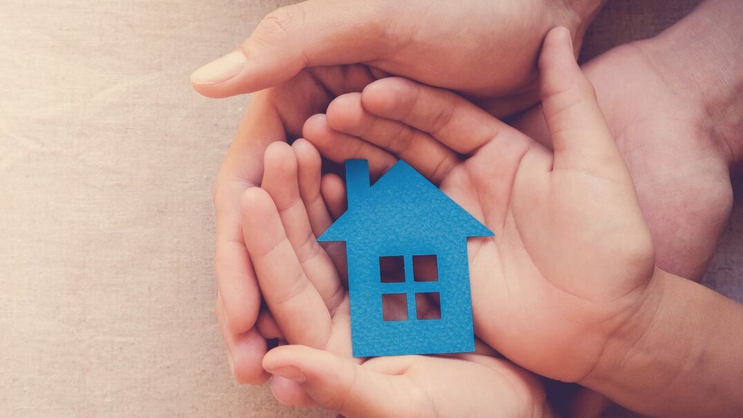 A adult and a child's hands holding a blue house cut out