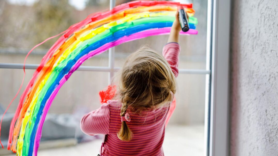 young girl drawing a rainbow on a glass window